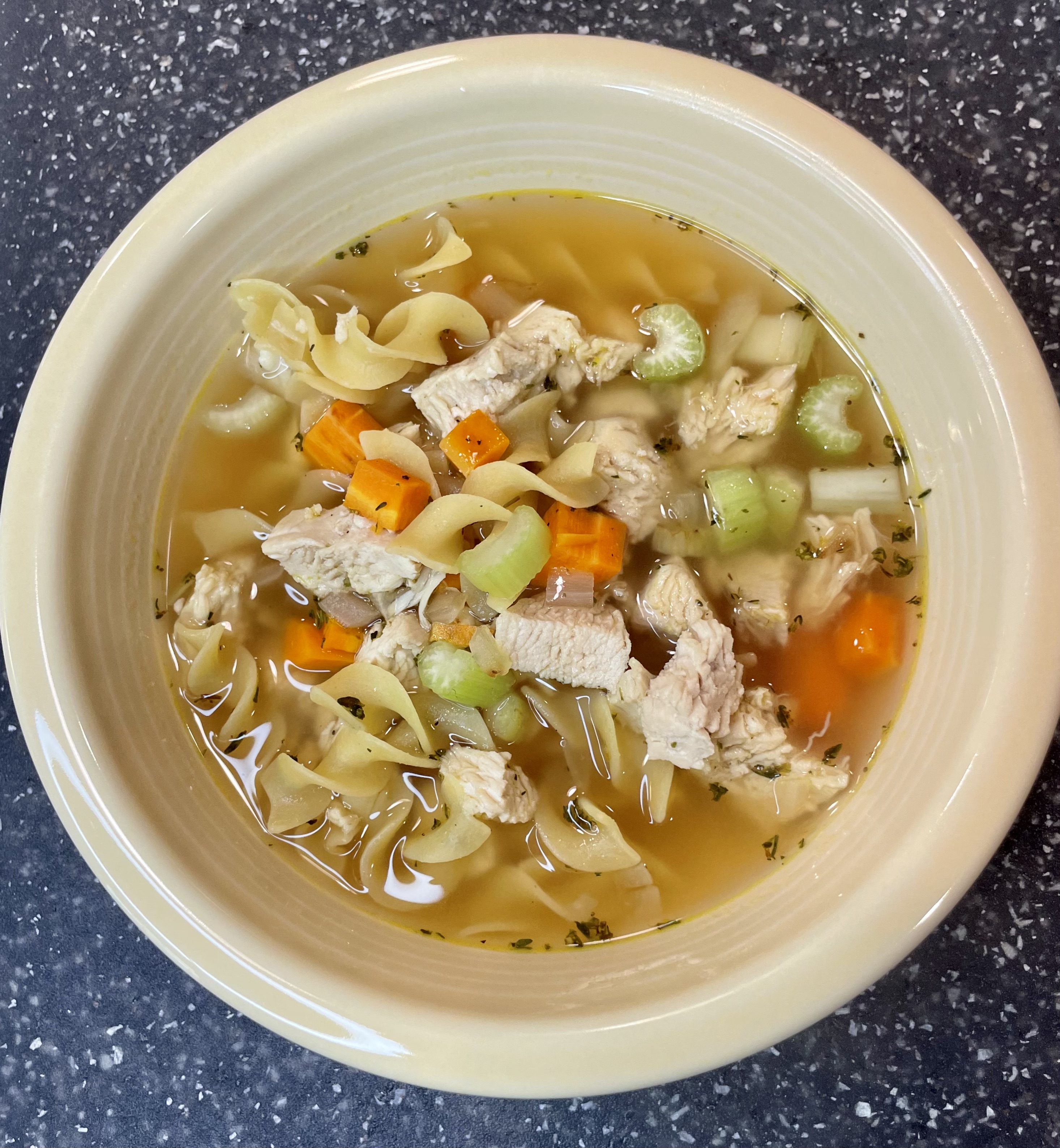Classic chicken noodle soup with carrots, celery, and noodles in a creamy colored bowl