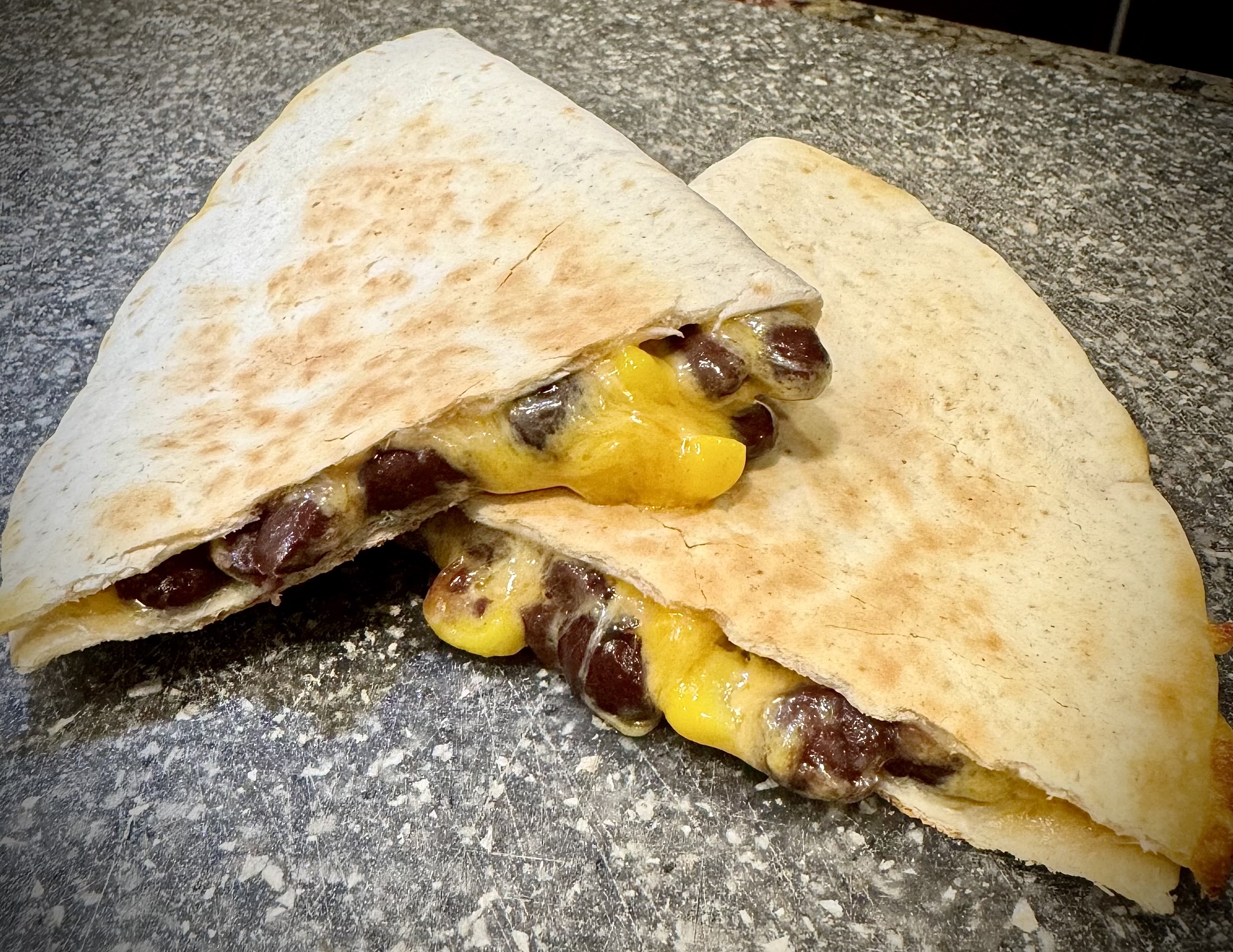 Crispy black bean and corn quesadilla cut in half on a gray cutting board.