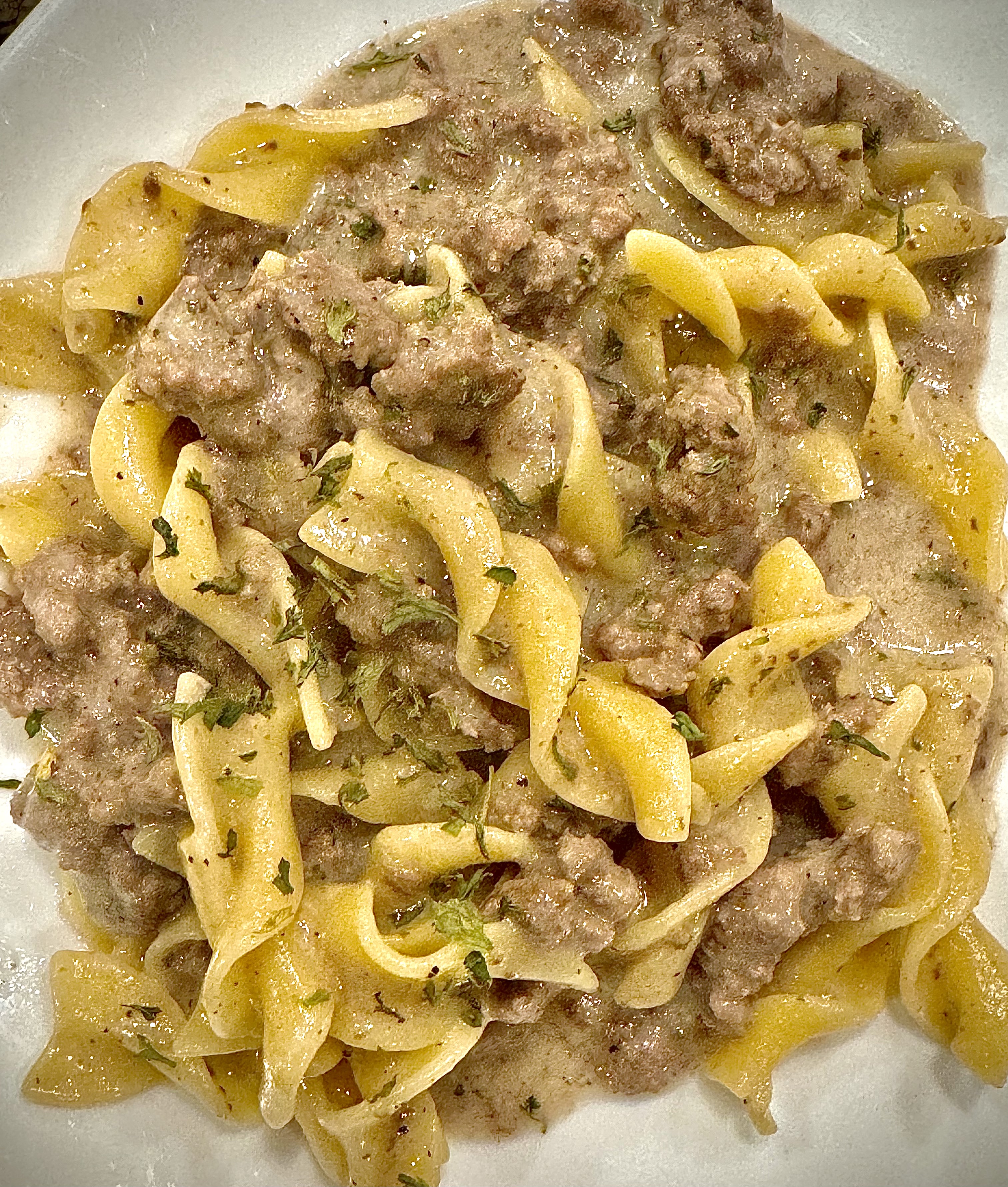 An easy ground beef recipe called Easy Beef Stroganoff with a creamy sauce, egg noodles, and ground beef on a white plate.