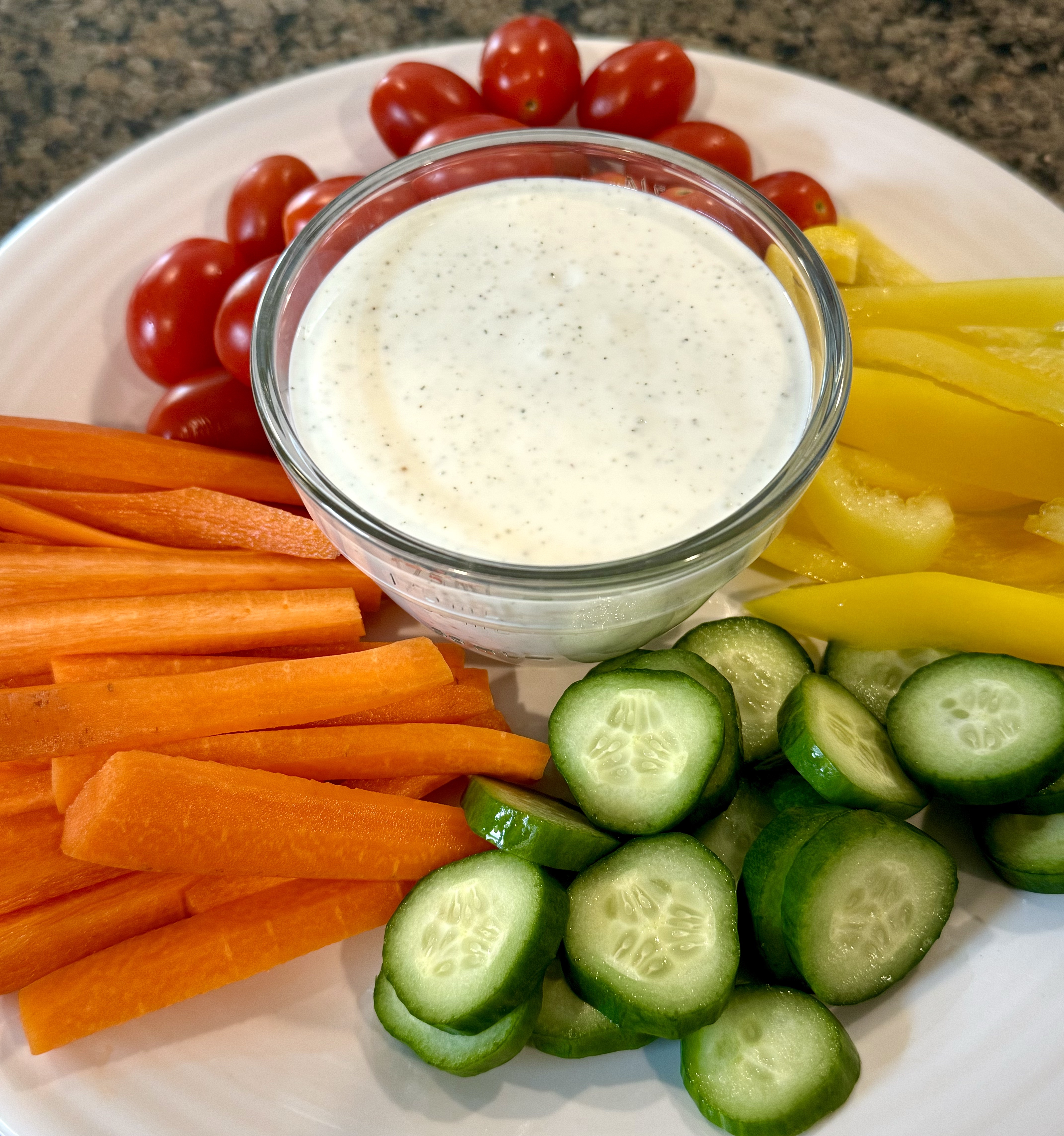 Cottage cheese ranch in a glass bowl surrounded by vegetables like tomatoes, bell peppers, and cucumbers