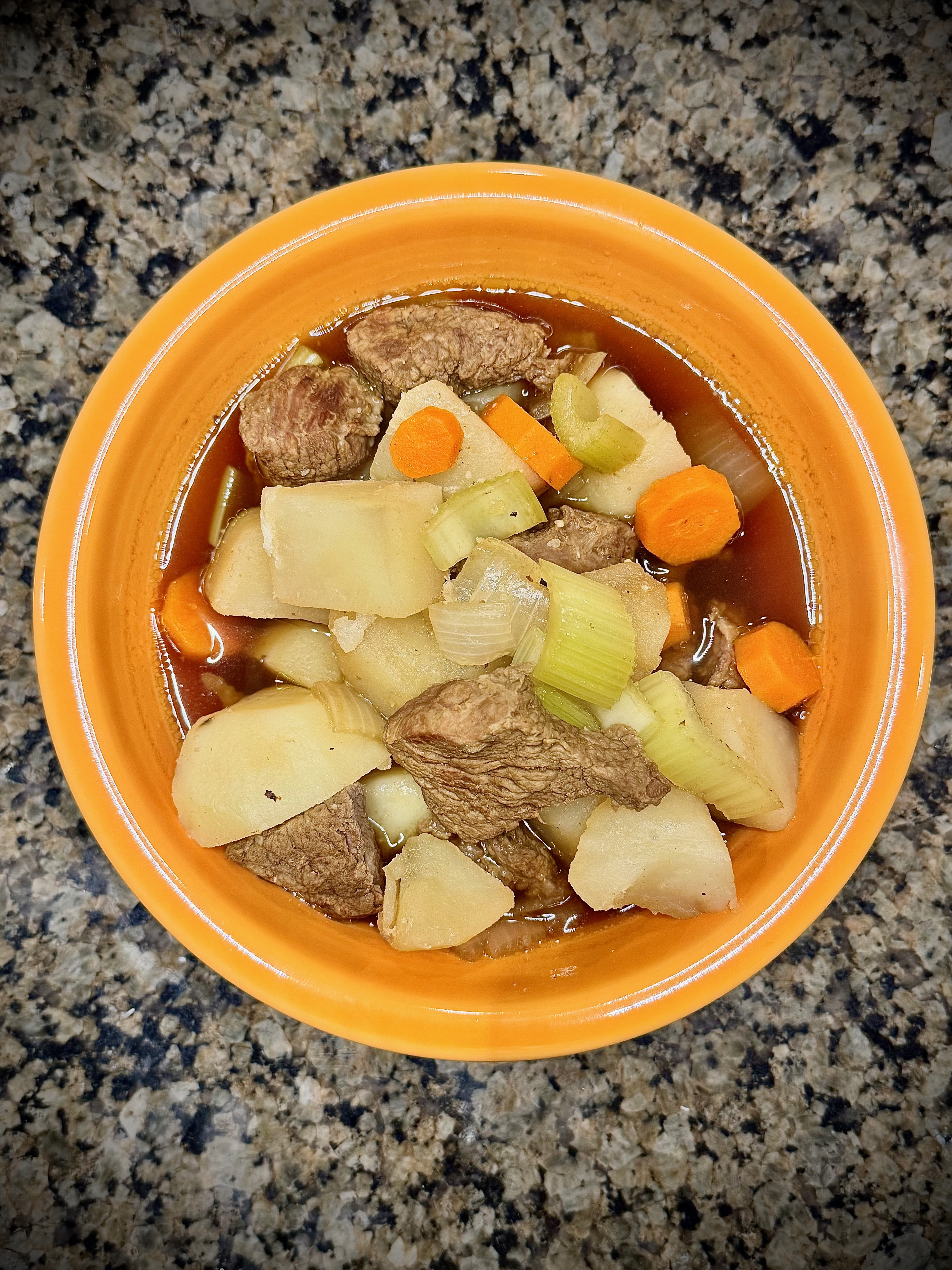 A hearty bowl of beef stew with tender meat, carrots, and potatoes in a rich brown broth.